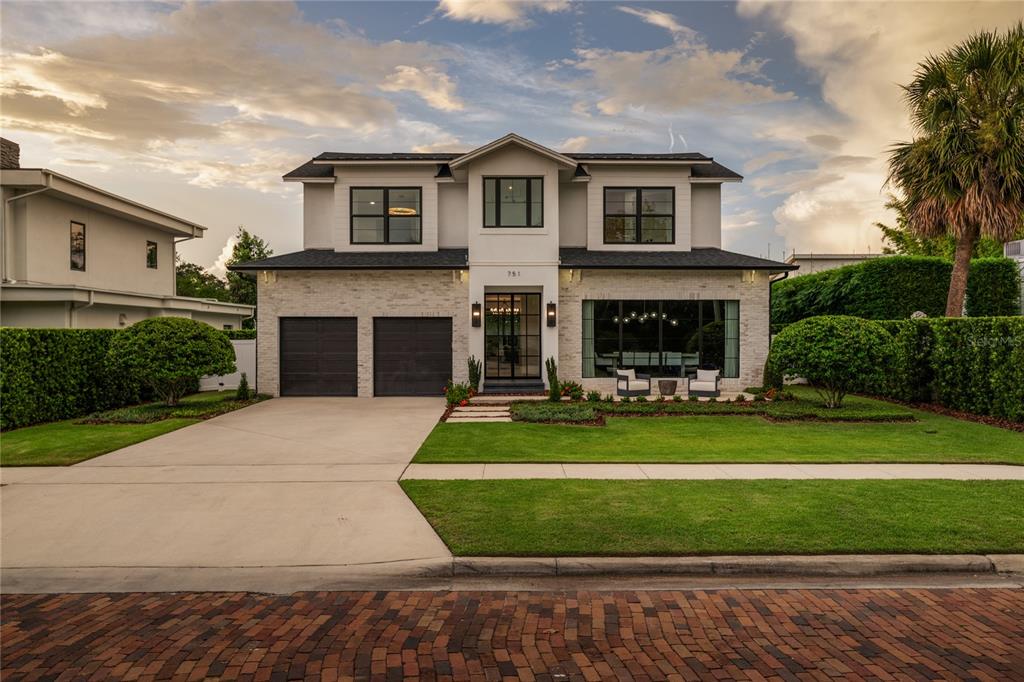 A two-story house with a white stone facade, dark garage doors, and a manicured lawn — 751 PANSY AVENUE, WINTER PARK, FL