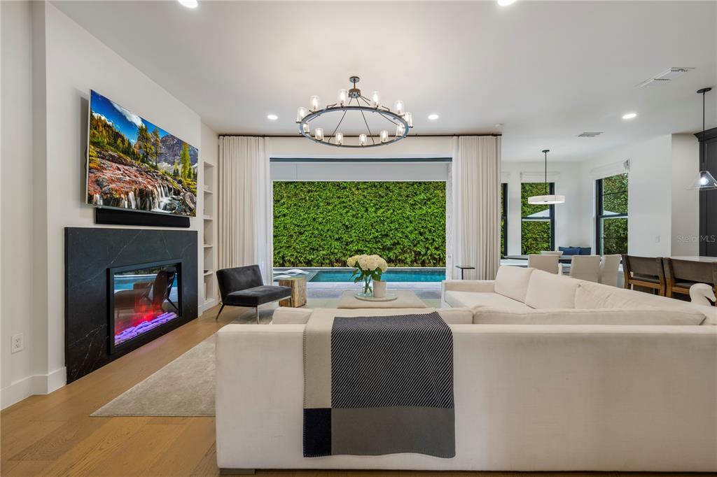 A modern living room features a black fireplace, large sectional sofa, and sliding doors to a pool — 751 PANSY AVENUE, WINTER PARK, FL