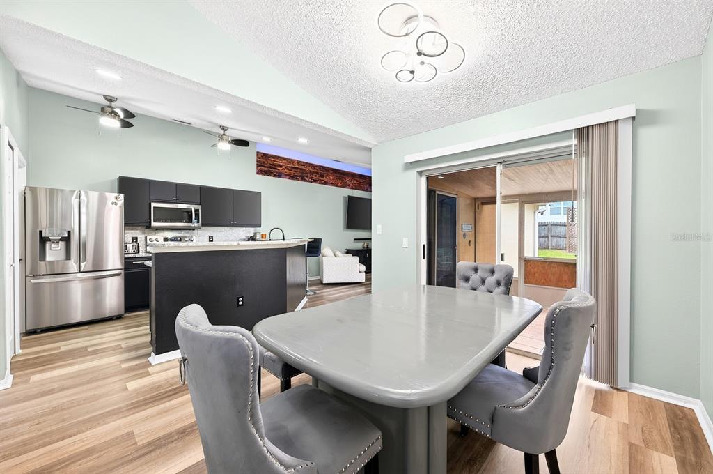 A dining area with a grey table and chairs opens to a kitchen and patio — 3147 UTAH DRIVE, DELTONA, FL