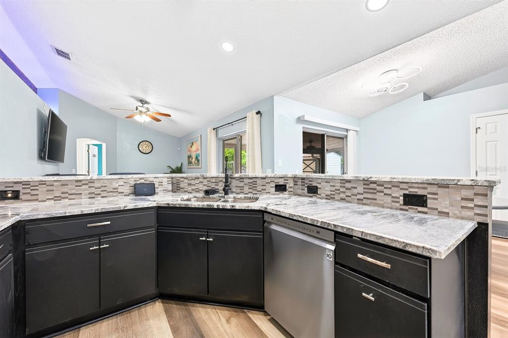 A kitchen features black cabinets, granite countertops, a tiled backsplash, and stainless steel appliances — 3147 UTAH DRIVE, DELTONA, FL