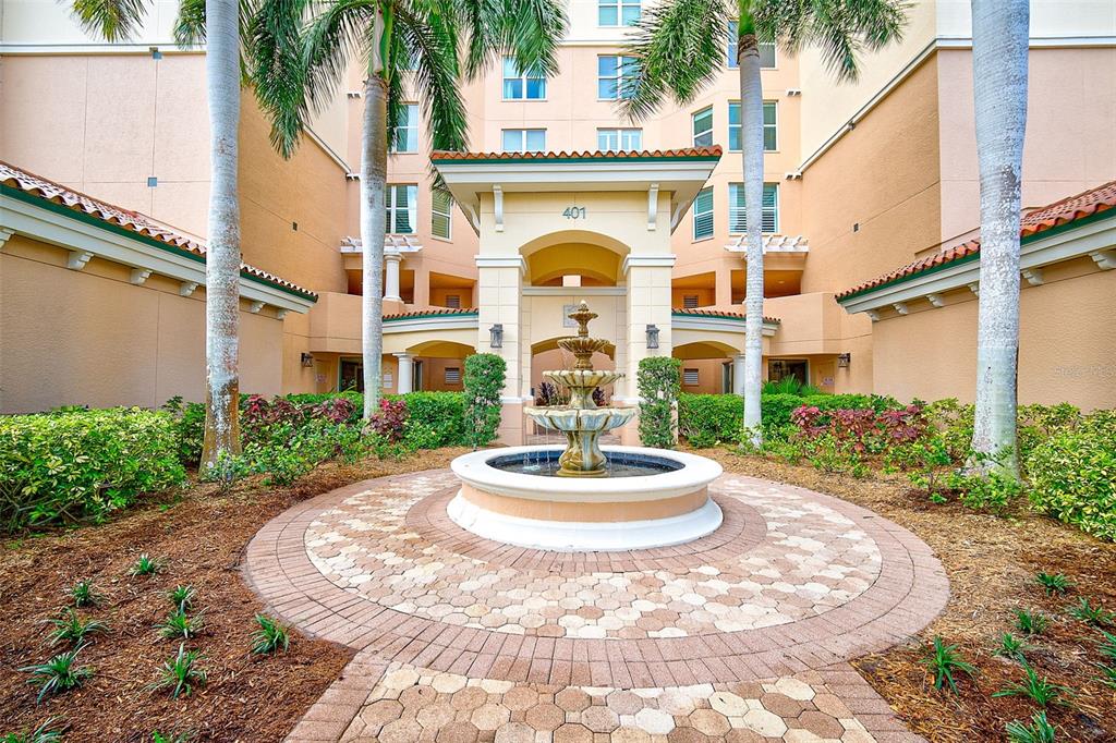 A tiered stone fountain sits in a circular brick courtyard before a multi-story building entrance — 401 N POINT ROAD UNIT 1001, OSPREY, FL