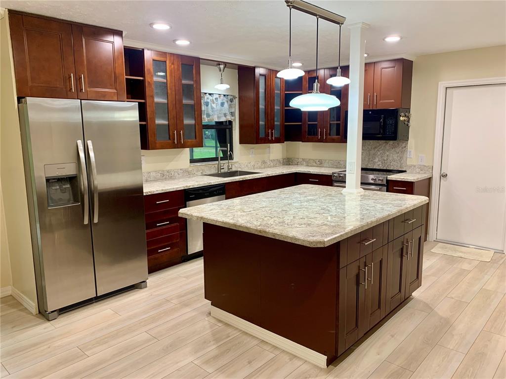 A kitchen features dark wood cabinets, stainless steel appliances, a granite island, and light flooring — 660 SUNDANCE TRAIL, WIMAUMA, FL