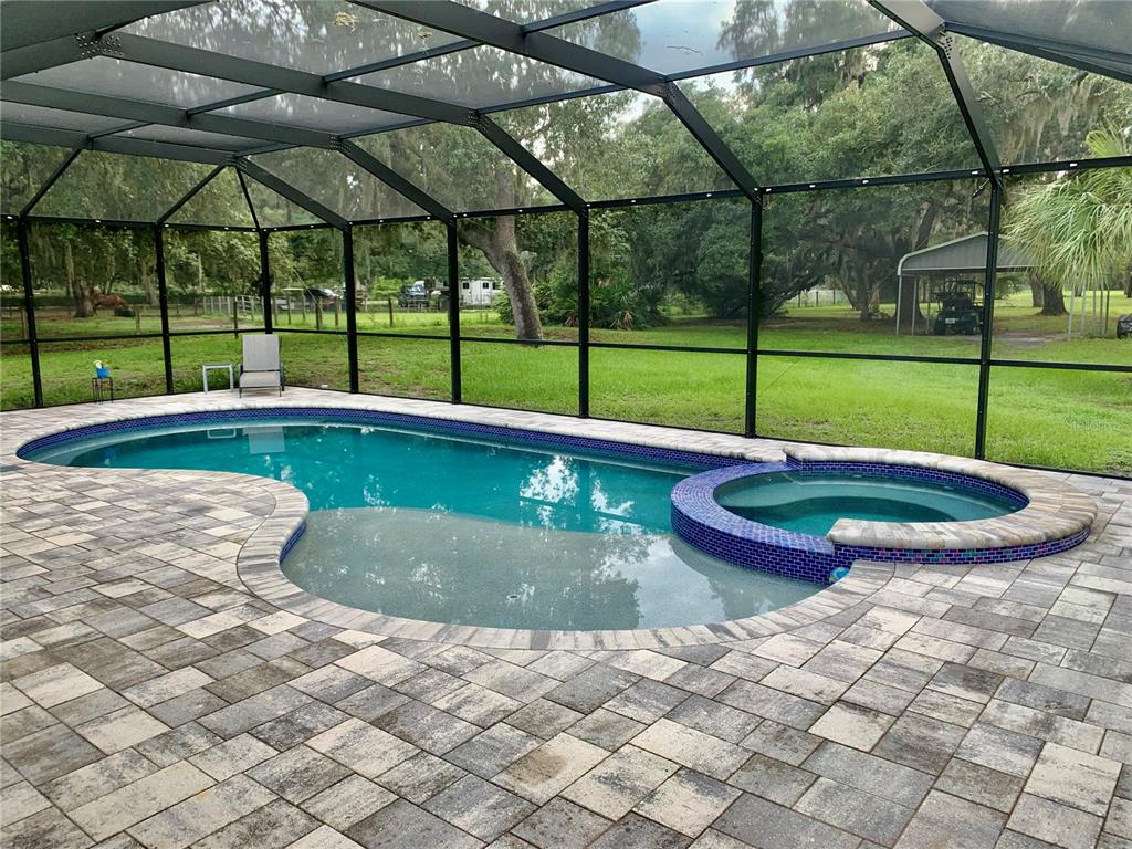 A screened-in swimming pool and spa with paver decking overlook a grassy backyard with trees — 660 SUNDANCE TRAIL, WIMAUMA, FL