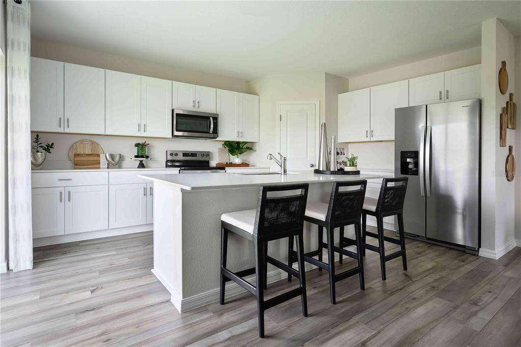 A modern kitchen features white cabinets, a central island with three stools, and stainless appliances — 36552 SAGEMOOR DRIVE, ZEPHYRHILLS, FL