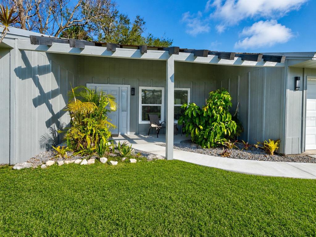 A gray house exterior features a covered entryway with a pergola and landscaped front yard — 101 SEA STREET, NEW SMYRNA BEACH, FL