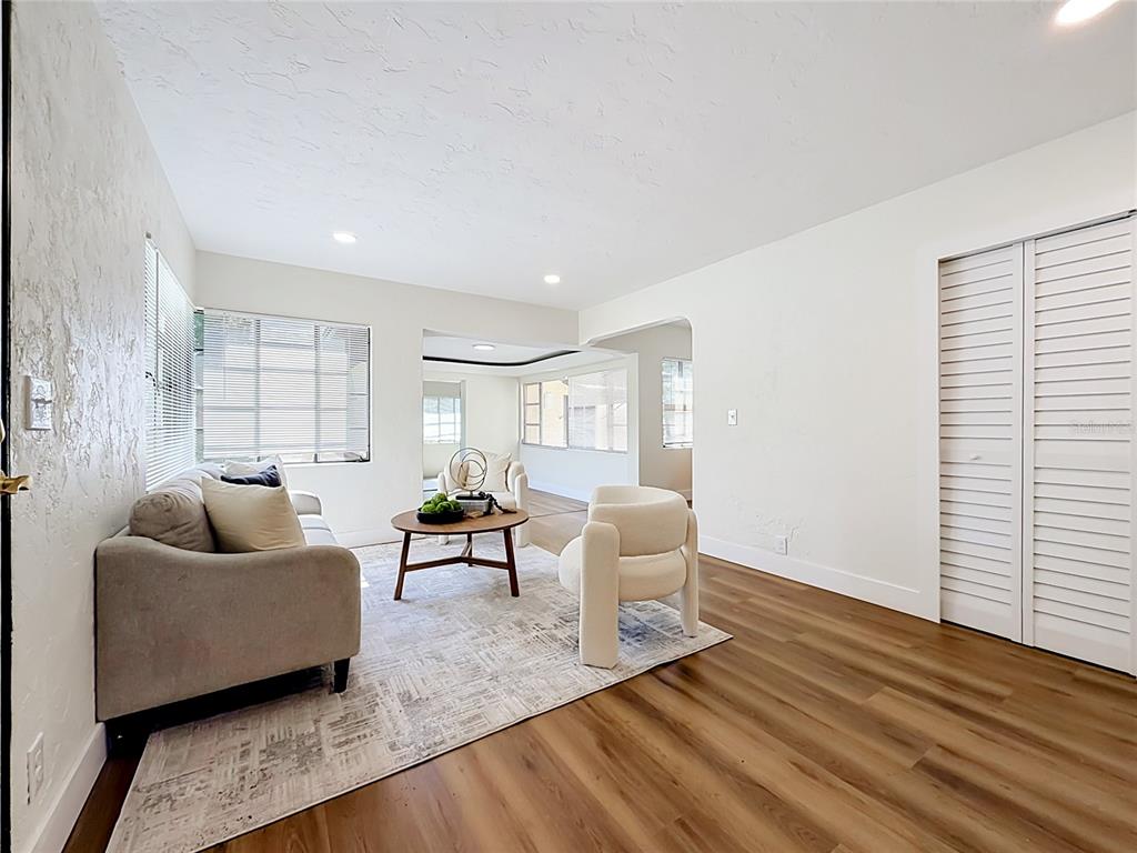 A living room with white walls, wood-look flooring, a gray sofa, and two cream chairs — 948 NE 6TH ST, OCALA, FL