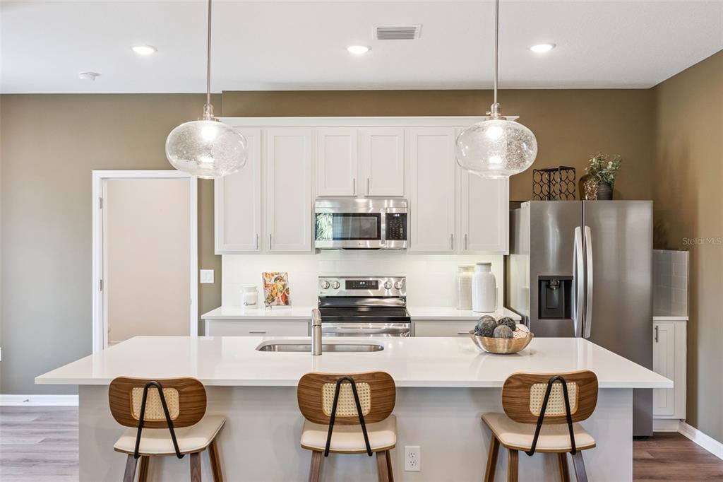 A modern kitchen features white cabinets, stainless steel appliances, a quartz island, and three stools — 2303 RED PINE COURT, EUSTIS, FL