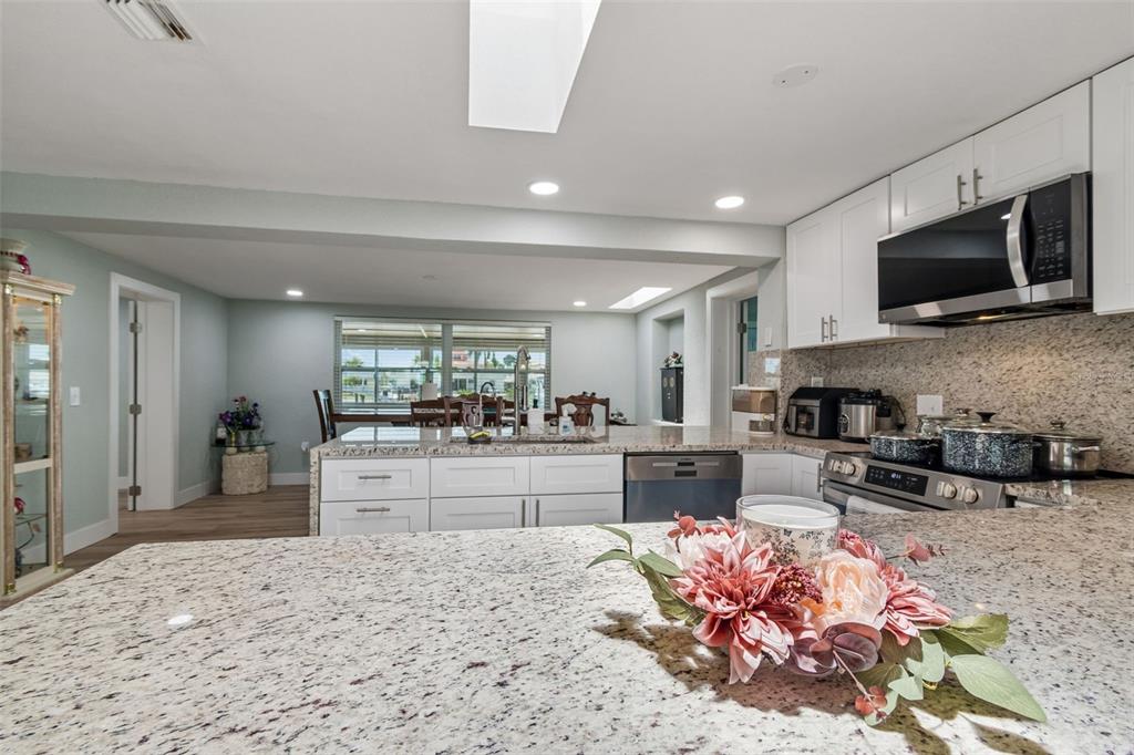 A kitchen with white cabinets, granite countertops, and a dining area in the background — 12617 4TH ISLE, HUDSON, FL