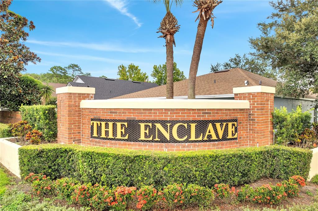 A brick monument sign for The Enclave stands in front of a house and landscaping — 3030 HOLLAND DRIVE, ORLANDO, FL