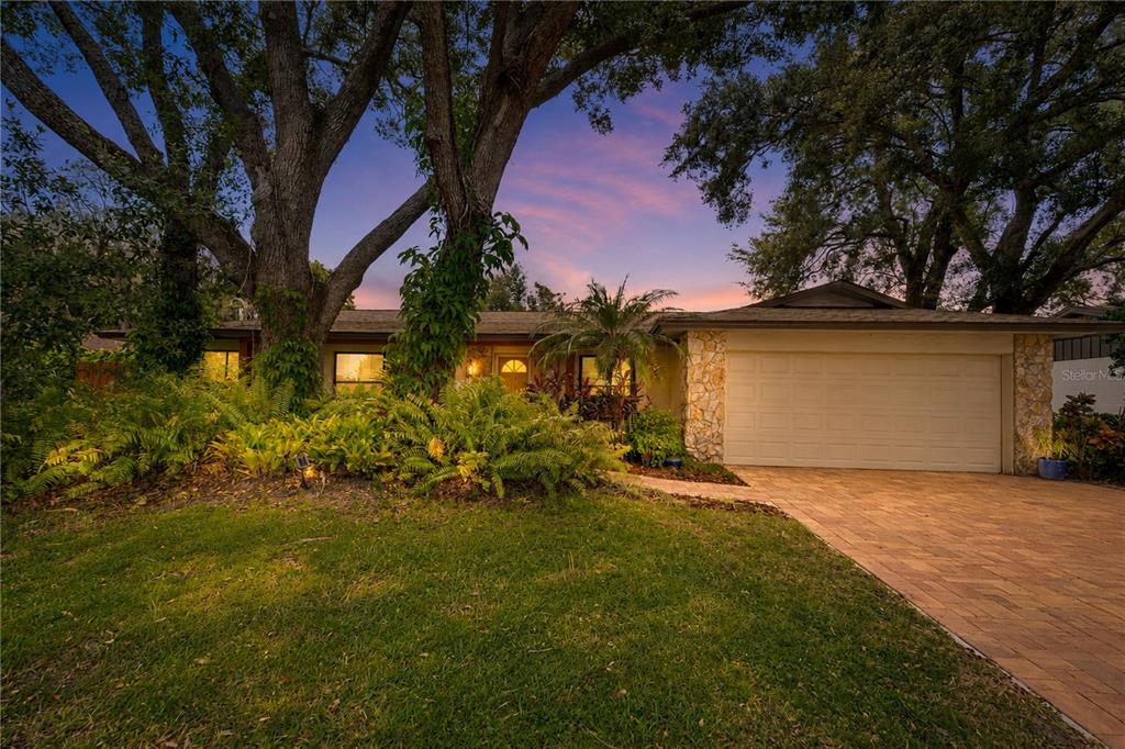 A single-story house with a stone facade, a two-car garage, and large trees in front — 3823 QUANDO DRIVE, BELLE ISLE, FL