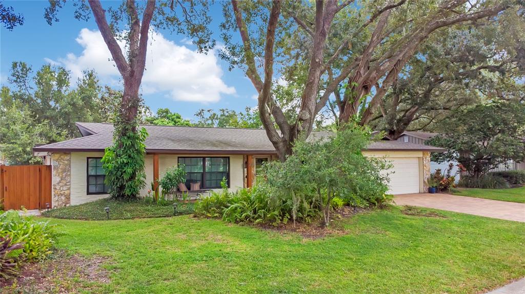 A single-story house with a stone facade, a two-car garage, and large trees in front — 3823 QUANDO DRIVE, BELLE ISLE, FL