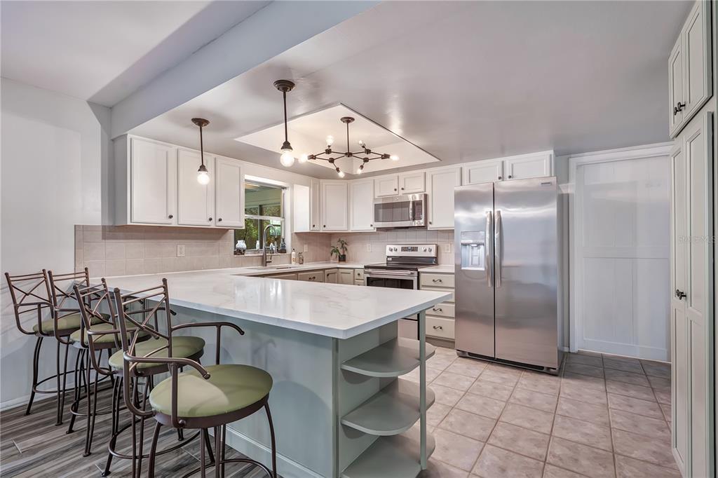 A kitchen features white cabinetry, a marble-topped island with bar stools, and stainless steel appliances — 3823 QUANDO DRIVE, BELLE ISLE, FL