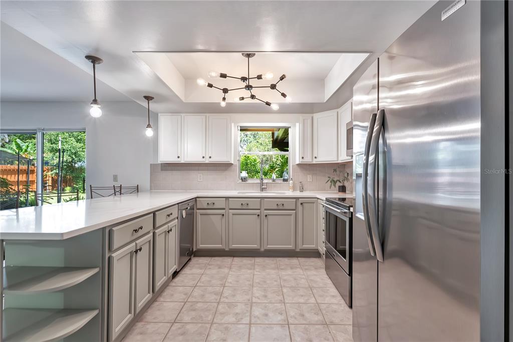 A kitchen features white upper cabinets, gray lower cabinets, stainless steel appliances, and a chandelier — 3823 QUANDO DRIVE, BELLE ISLE, FL