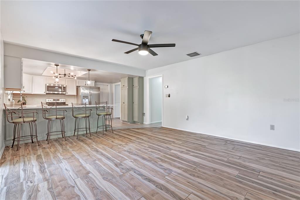 A kitchen with a breakfast bar and stools opens into a large, empty living area — 3823 QUANDO DRIVE, BELLE ISLE, FL