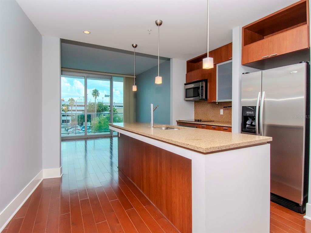 A modern kitchen features a granite-topped island, stainless steel appliances, and wood flooring — 912 CHANNELSIDE DRIVE UNIT 2311, TAMPA, FL