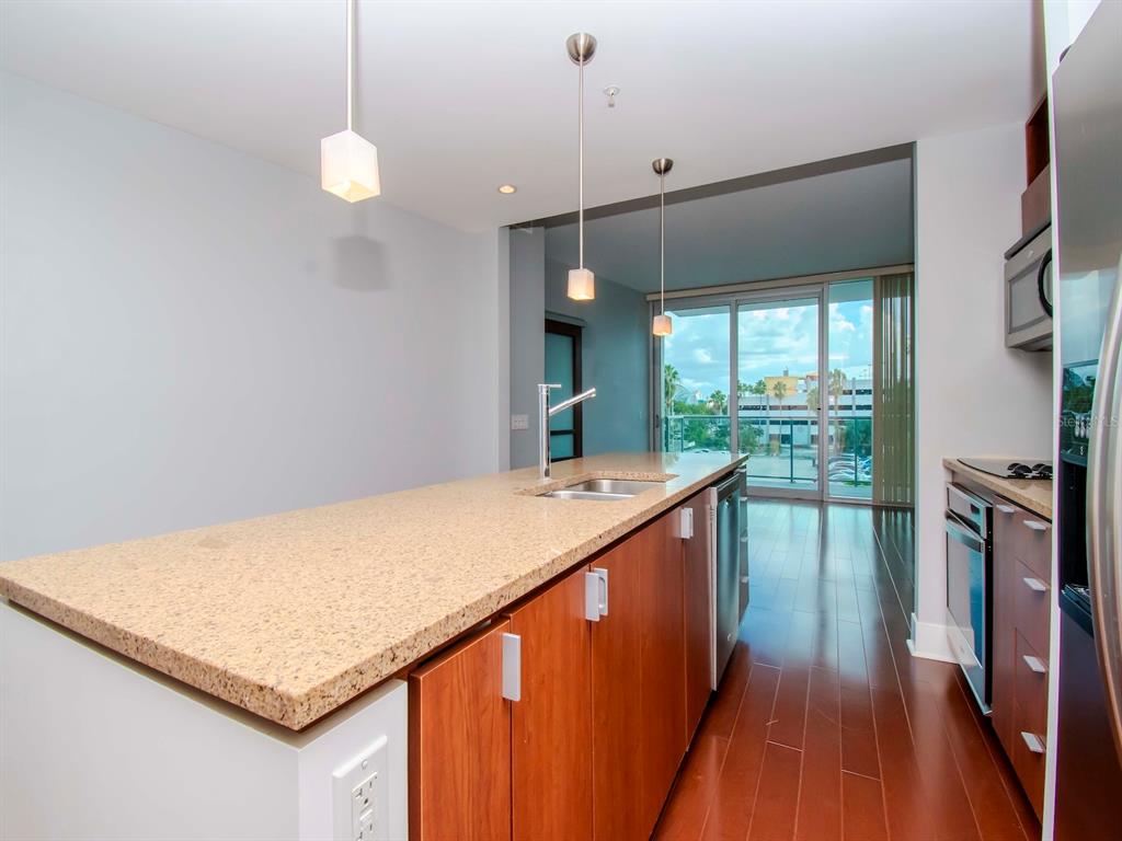 A kitchen with a granite-topped island, wood cabinets, and stainless steel appliances overlooking a balcony — 912 CHANNELSIDE DRIVE UNIT 2311, TAMPA, FL
