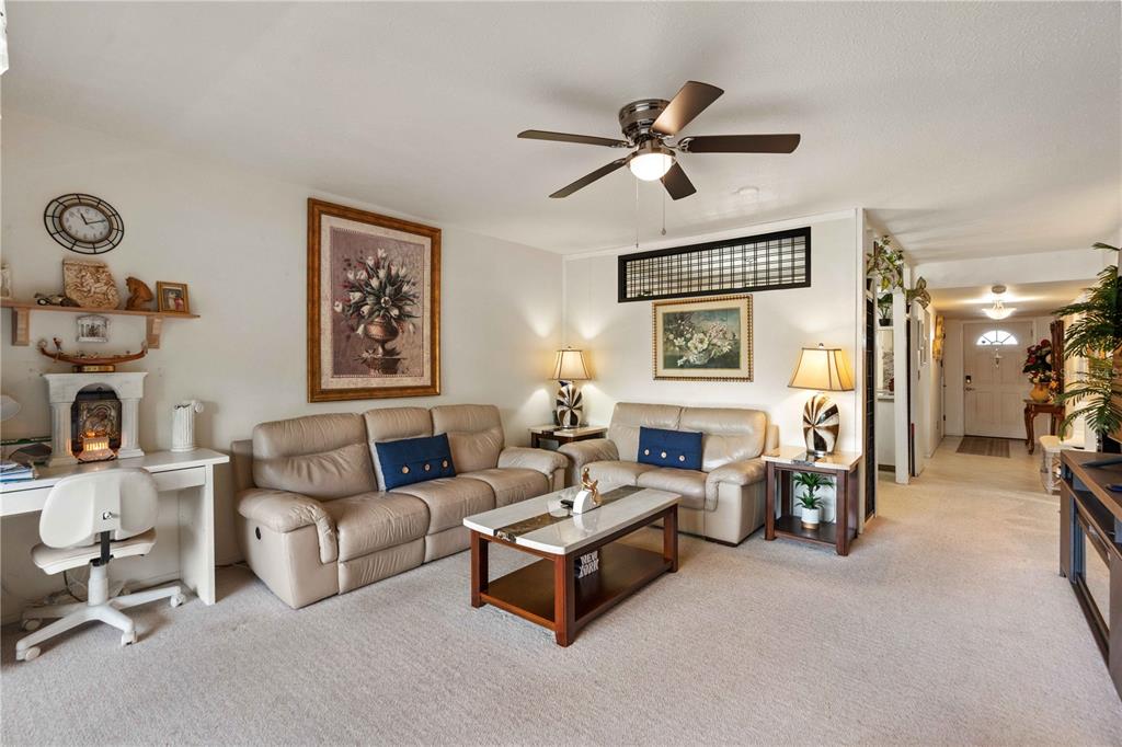 A living room features a television, coffee table, beige armchair, and sliding glass doors — 7623 RADCLIFFE CIRCLE UNIT 211A, PORT RICHEY, FL