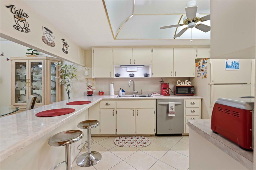 A kitchen features white cabinetry, tile flooring, a breakfast bar, and a ceiling fan — 7623 RADCLIFFE CIRCLE UNIT 211A, PORT RICHEY, FL