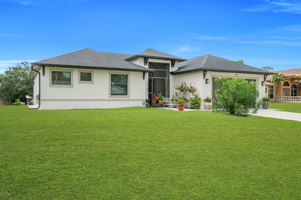 A single-story house with a white stucco exterior, dark roof, and a large front lawn — 609 CLAYTON AVENUE, LEHIGH ACRES, FL