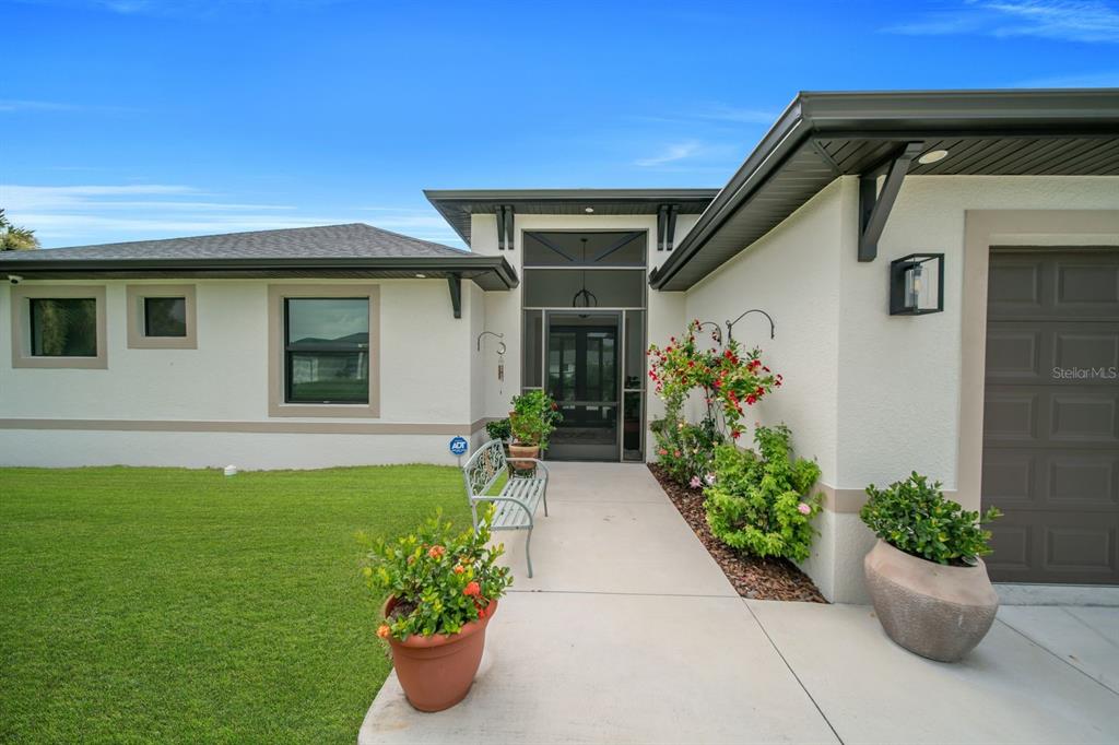 The exterior of a single-story house features a screened entryway, a concrete walkway, and landscaping — 609 CLAYTON AVENUE, LEHIGH ACRES, FL