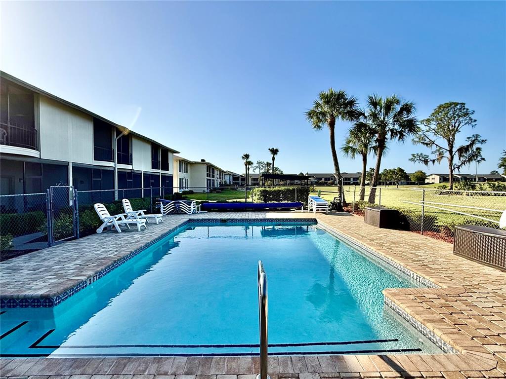 A rectangular swimming pool sits on a brick patio beside a multi-story apartment building — 3635 EDGEWATER DRIVE UNIT 3635, SEBRING, FL