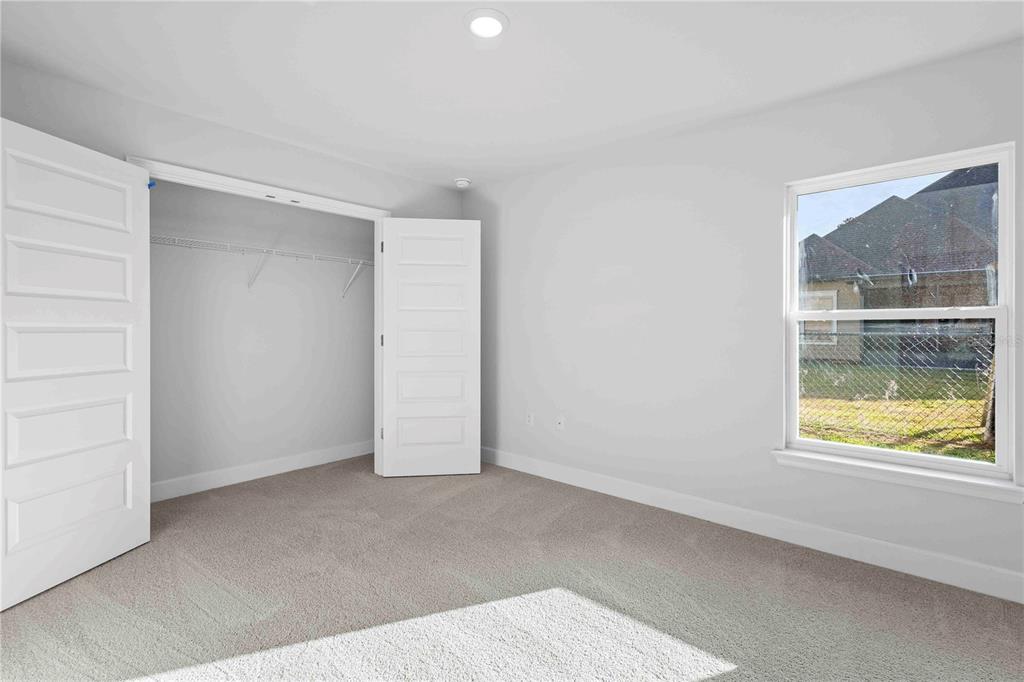 An empty bedroom features light gray walls, beige carpeting, a white closet, and a window — 483 SW BELLFLOWER DRIVE, LAKE CITY, FL