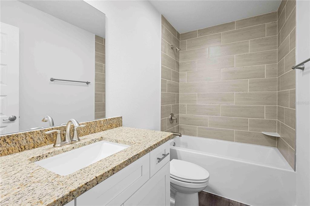 A bathroom features a granite vanity, white cabinet, and a tub with wood-look tile surround — 483 SW BELLFLOWER DRIVE, LAKE CITY, FL