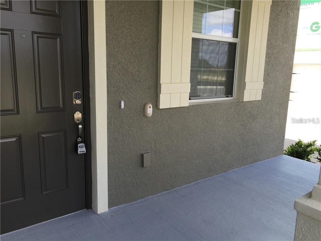A dark front door with a keypad lock sits beside a window on a porch — 13048 GARRIDAN AVENUE, WINDERMERE, FL