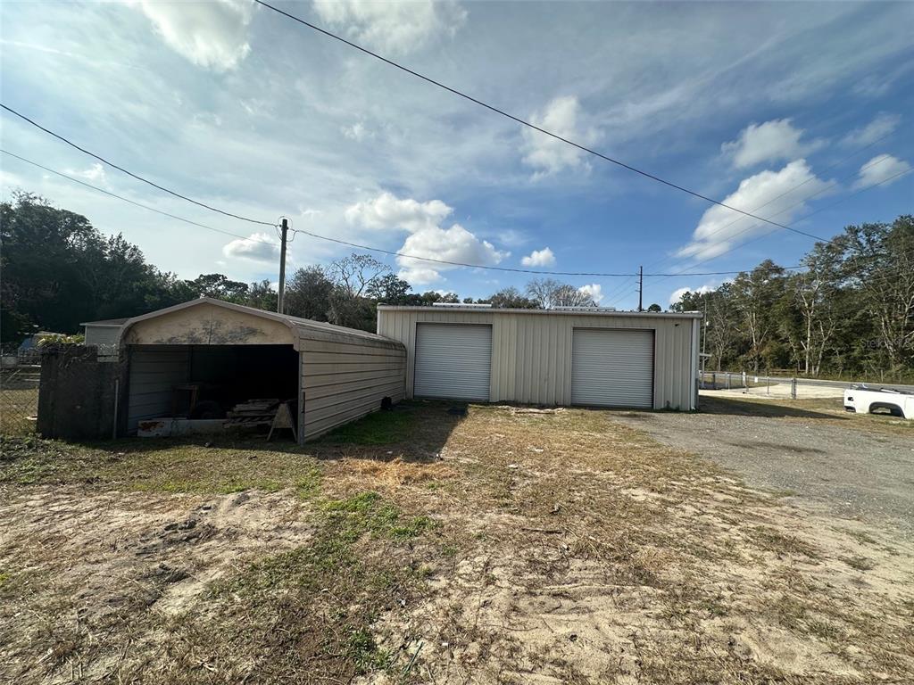 An exterior view of a metal workshop building with two roll-up doors and an attached carport — 7160 NE 7TH STREET, OCALA, FL