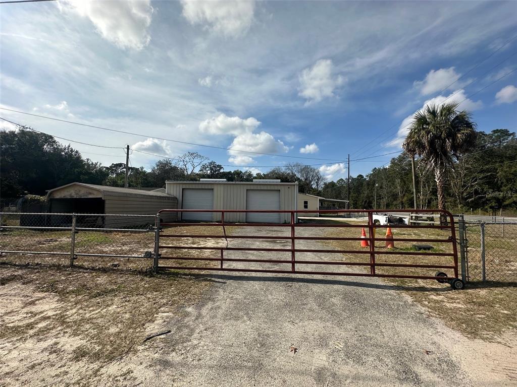 A metal workshop building with two roll-up doors sits behind a red metal gate — 7160 NE 7TH STREET, OCALA, FL