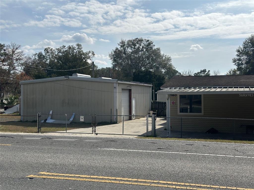 A metal warehouse building sits next to a small house behind a chain-link fence — 7160 NE 7TH STREET, OCALA, FL