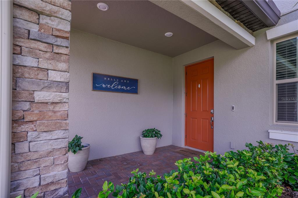 A front entryway features a bright orange door, stone siding, and two potted plants — 24893 LAMBRUSCO LOOP, LUTZ, FL