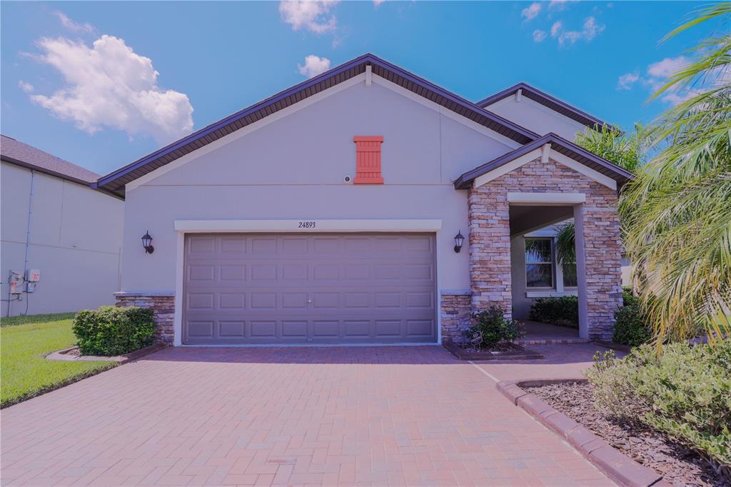A suburban house exterior features a brick paver driveway, a two-car garage, and stone accents — 24893 LAMBRUSCO LOOP, LUTZ, FL