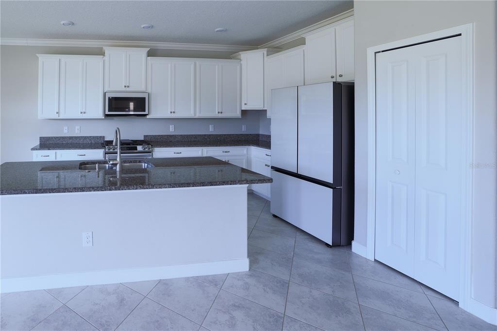A kitchen features white cabinets, granite countertops, a center island, and a stainless steel refrigerator — 24893 LAMBRUSCO LOOP, LUTZ, FL
