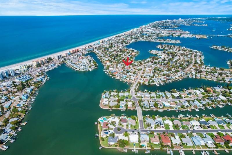An aerial view shows a coastal neighborhood with houses situated along canals and the ocean — 421 VIRGINIA AVENUE, MADEIRA BEACH, FL