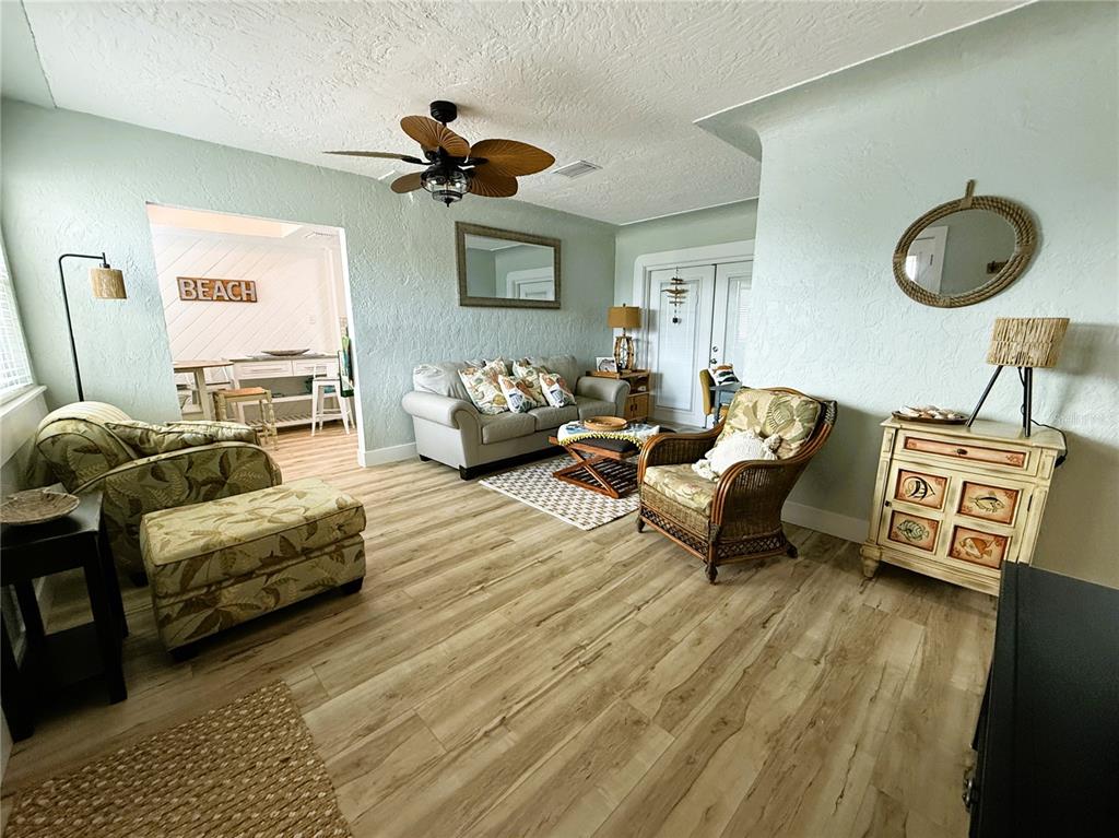 A living room features light green walls, wood-look flooring, a ceiling fan, and coastal-style furniture — 421 VIRGINIA AVENUE, MADEIRA BEACH, FL