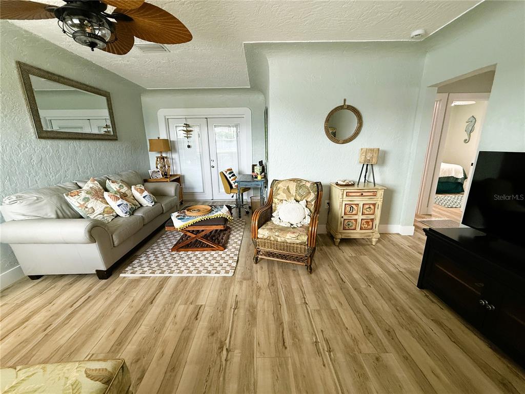 A living room features light wood-look flooring, a beige sofa, and a wicker accent chair — 421 VIRGINIA AVENUE, MADEIRA BEACH, FL