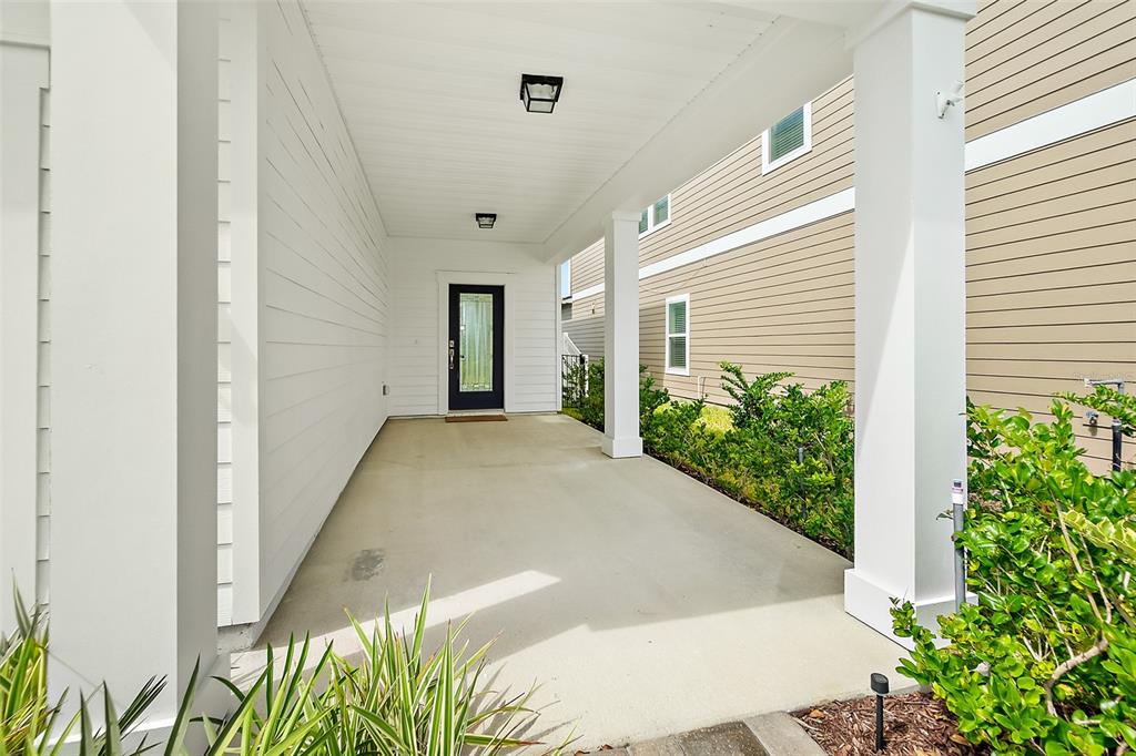 A covered concrete porch leads to a dark-framed front door of a tan house — 542 SILVER LANDING DRIVE, ST AUGUSTINE, FL