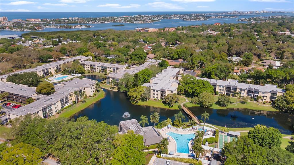 An aerial view of a multi-building apartment complex with a central pond and swimming pool — 14130 ROSEMARY LANE UNIT 1318, LARGO, FL