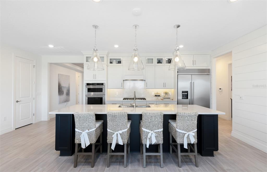 A modern kitchen features a dark island with four woven stools and white cabinetry — 285 CRYSTAL WOOD DRIVE, WINTER GARDEN, FL