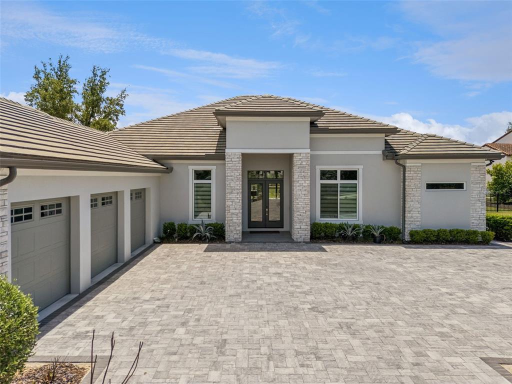 A single-story house with a paved driveway, three-car garage, and stone-accented entryway — 15220 PENDIO DRIVE, BELLA COLLINA, FL