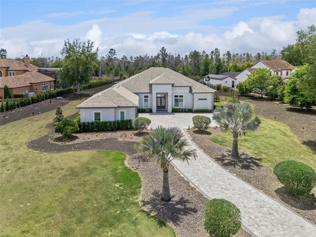 An aerial view shows a single-story house with a paver driveway and palm trees — 15220 PENDIO DRIVE, BELLA COLLINA, FL