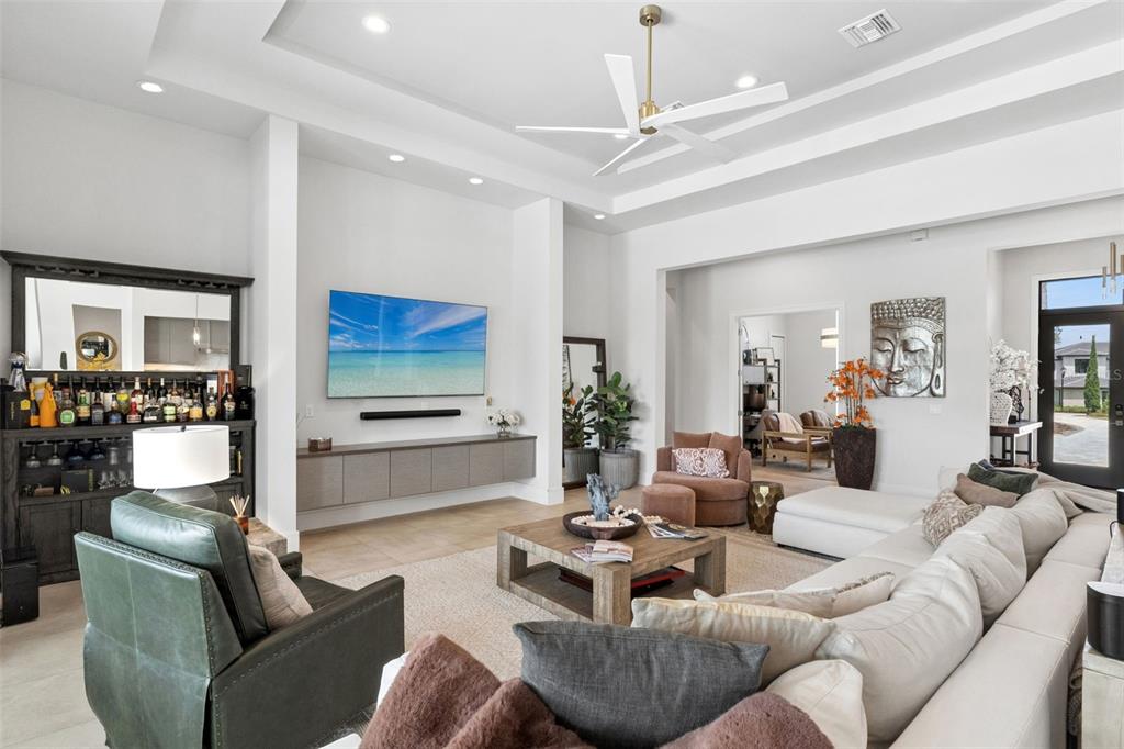 A spacious living room features a tray ceiling, a wall-mounted television, and a wet bar — 15220 PENDIO DRIVE, BELLA COLLINA, FL