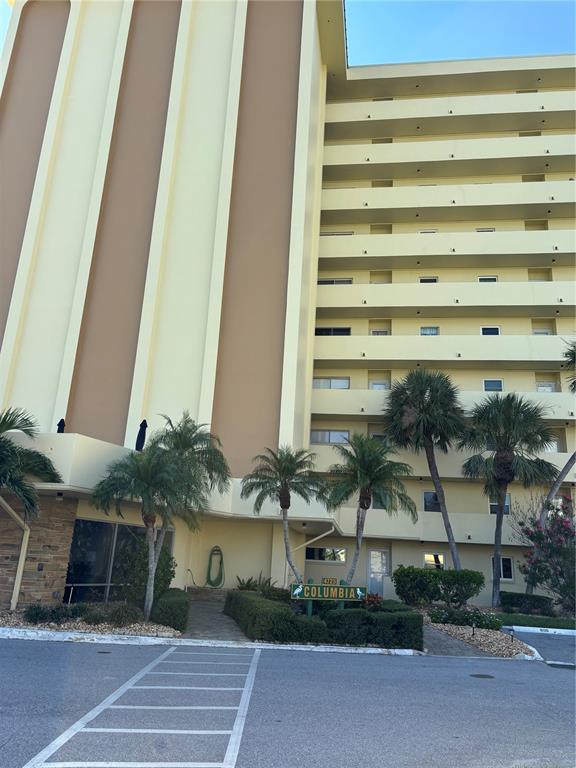 A multi-story yellow apartment building features a ground-level entrance with palm trees and landscaping — 4725 COVE CIRCLE UNIT 104, MADEIRA BEACH, FL