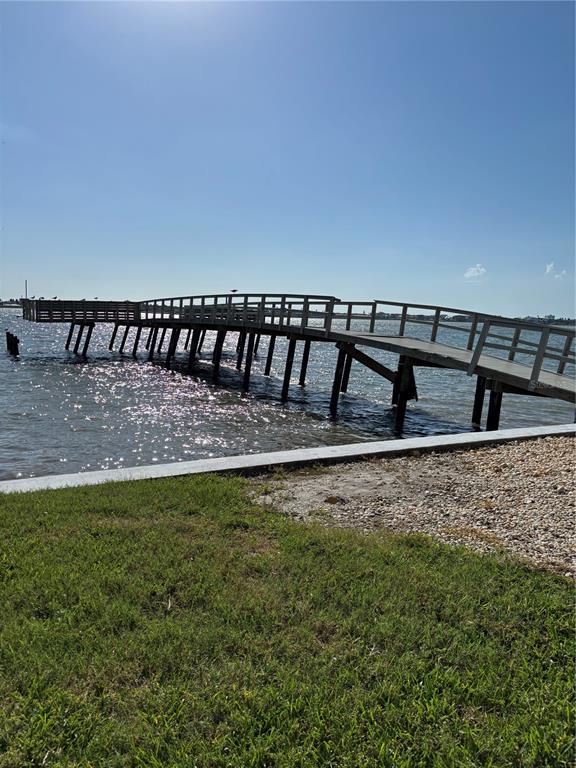 A wooden pier extends over the water from a grassy shoreline under a clear sky — 4725 COVE CIRCLE UNIT 104, MADEIRA BEACH, FL