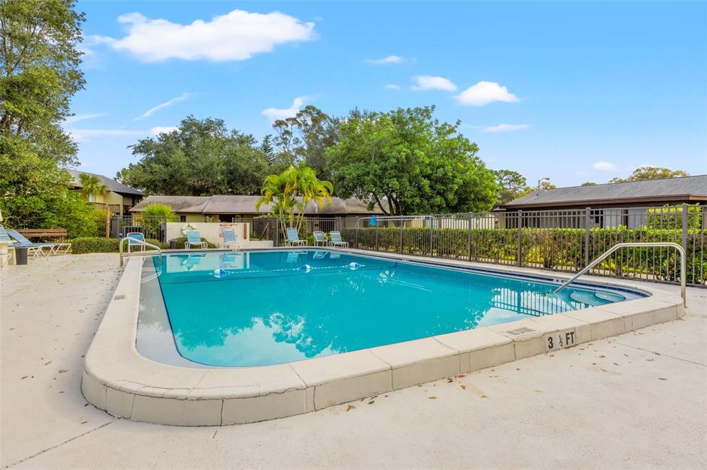 An outdoor swimming pool with a shallow end depth marker is surrounded by a metal fence — 4215 E BAY DRIVE UNIT 1702F, CLEARWATER, FL