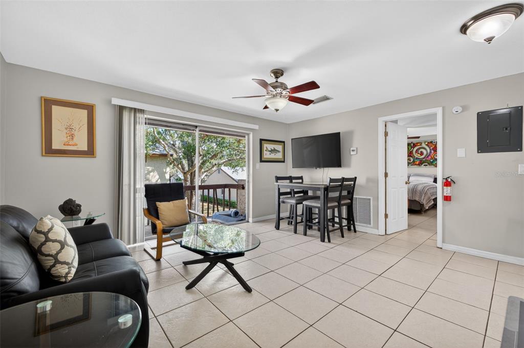 A living room with tile floors, a black sofa, a dining set, and a sliding door — 4215 E BAY DRIVE UNIT 1702F, CLEARWATER, FL
