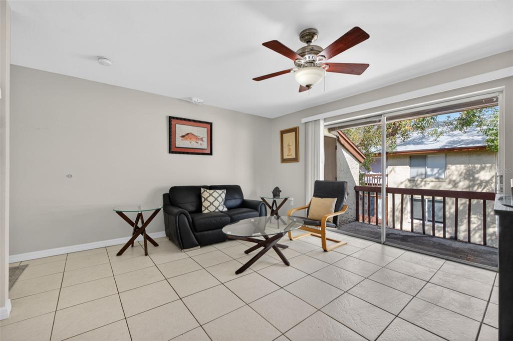 A living room with tile floors, a black sofa, a glass coffee table, and a balcony — 4215 E BAY DRIVE UNIT 1702F, CLEARWATER, FL