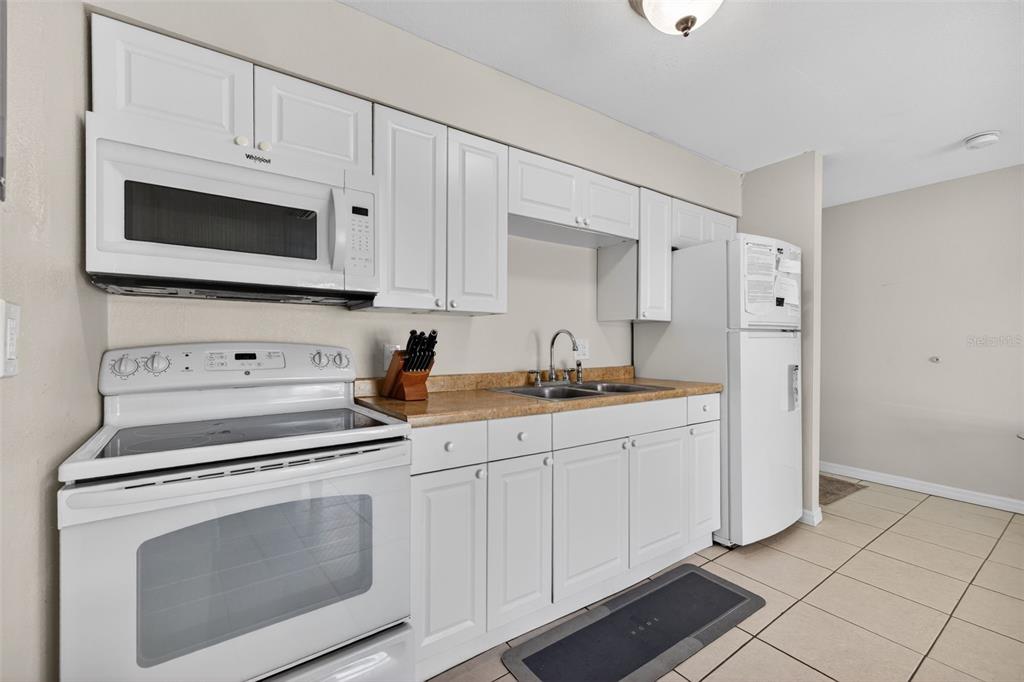 A kitchen features white cabinets, white appliances, and tan countertops over tiled flooring — 4215 E BAY DRIVE UNIT 1702F, CLEARWATER, FL