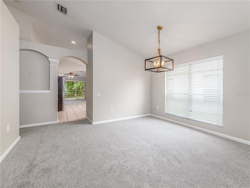 A dining room with gray carpet, light walls, a modern chandelier, and a large window — 25342 LEXINGTON OAKS BOULEVARD, WESLEY CHAPEL, FL